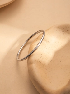 Polished silver stainless steel bangle with hinge closure on ceramic tray