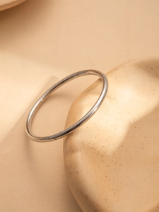 Polished silver stainless steel minimalist bracelet on a cream aesthetic tray