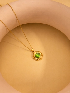 Detail van gouden titanium ketting met ronde groene kattenoog hanger op beige achtergrond