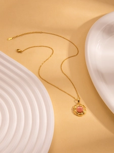 Macro-opname van gouden zonnebloemketting met roze edelsteen op wit keramisch bord