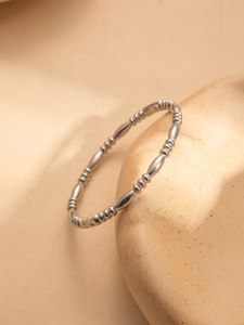Detail view of a minimalist silver beaded steel bracelet draped on a ceramic prop