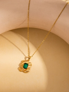 Macro-opname van gouden titanium stalen ketting met een rechthoekige groene edelsteen