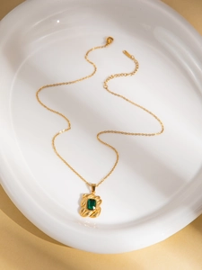 Detailopname van gouden ketting met groene smaragd hanger op een wit keramisch dienblad