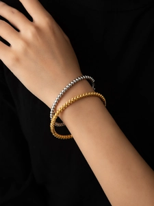 Detailed shot of layered gold textured and silver polished bead bracelets on wrist