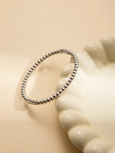 Detail of silver beaded stainless steel open cuff bracelet on a ceramic tray
