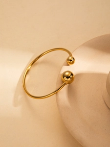 Detail of minimalist gold open bangle featuring polished spheres on a beige stand