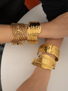 Close-up of four bold gold-plated cuff bracelets in varied artistic textures on wrist
