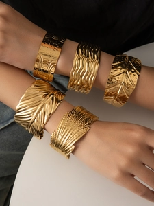 Detail of stacked gold plated titanium steel bangles with feather and wave textures