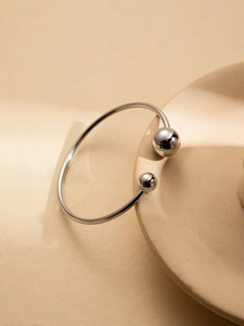 Macro detail of silver geometric open cuff bracelet with metallic beads on ceramic plate