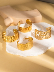 Detail of four gold-plated stainless steel cuff bracelets with wave and hammered textures