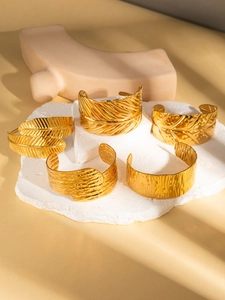 Close-up of five gold plated titanium steel bangles with feather and textured patterns