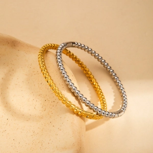 Elegant 18K gold plated twisted bangle and silver beaded bracelet set on ceramic tray