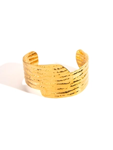 Detail of wide golden hammered cuff bracelet with elegant overlapping texture and metal finish