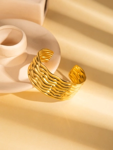 Macro detail of gold wide wave-patterned bangle with elegant shadows on beige surface