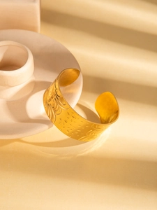 Detailed view of a wide gold-plated stainless steel cuff bracelet with embossed patterns