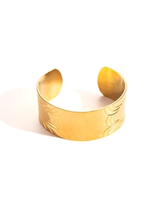 Detail showing gold cuff bracelet with hammered texture and engraved wave patterns