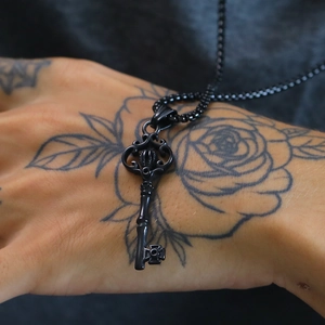 Close-up of gothic black crown key necklace pendant with rose tattoo background
