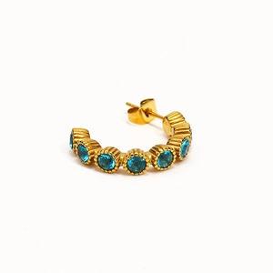 Détail d'une boucle d'oreille dorée en forme de C sertie de sept zircons bleu vif