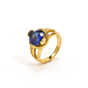 Macro detail of gold-plated ring featuring a large faceted blue gemstone and hollow band