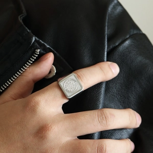 Macro detail of men's silver signet ring featuring a compass design on black leather jacket