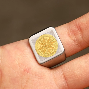 Macro detail of men's matte stainless steel signet ring with gold compass emblem