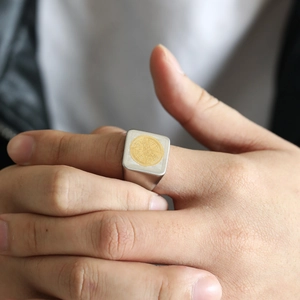 Close-up of a matte silver signet ring featuring a gold compass emblem on a model hand