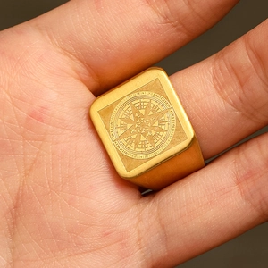 Close-up of golden square signet ring with compass engraving and brushed metal texture