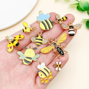 Detailed macro view of assorted gold-plated enamel bee charms held in hand for size reference