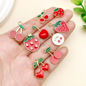 Detailed view of handmade strawberry and cherry alloy charms held in hand for scale