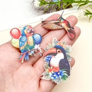 Gros plan de breloques d'oiseaux en acrylique avec perroquet et colibri en main