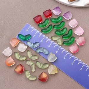 Colorful glass tulip and leaf beads for DIY jewelry making laid out on purple fabric