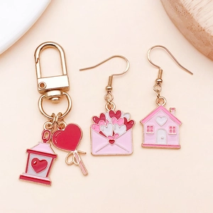 Detalle de dijes de corazón en esmalte rosa y aretes de casita para joyería artesanal