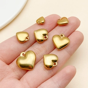 Polished gold heart pendants in various sizes held by hand for scale reference
