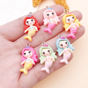 Close-up of resin mermaid pendants in various colors held in hand for DIY jewelry making