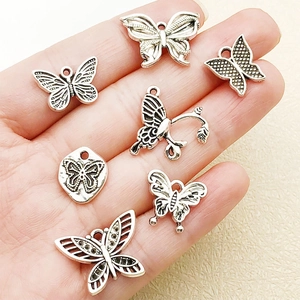 Detail view of assorted vintage silver butterfly charms held in hand for scale