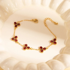 Dettaglio del bracciale a catena dorata con cinque quadrifogli di gemme rosse su vassoio