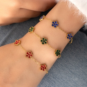 Nahaufnahme goldener Armbänder mit bunten Blumen-Kristallanhängern am Handgelenk