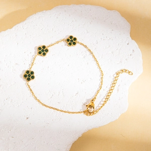 Detail eines goldenen Titanarmbands mit Blumenanhängern und grünen Kunststeinen