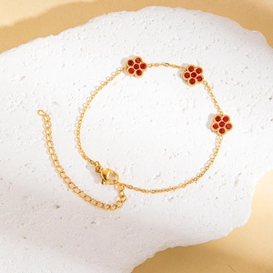 Detailaufnahme von goldenem Titanarmband mit roten Kristallblumen auf Steinhintergrund