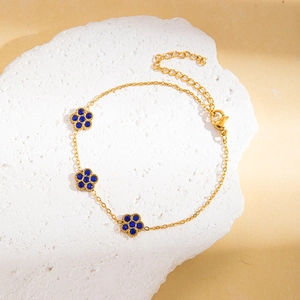 Detail eines goldenen Titan-Armbands mit blauen Strassblumen auf einem Steinuntergrund