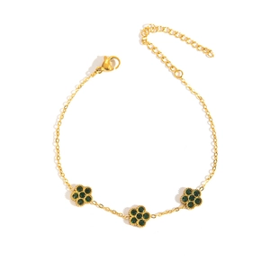 Detail eines Gold-Titanarmbands mit drei Blumenanhängern und grünen Kristallen