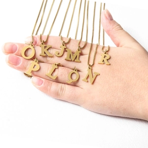 Close-up of gold uppercase initial necklaces with delicate box chains on a white background