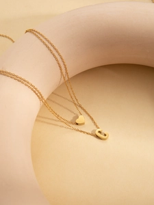 Close-up of a double-layered gold-plated necklace featuring a heart and letter C pendant