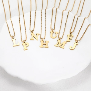 Gold titanium steel initial necklaces featuring letters L P N H U M F J on white ceramic