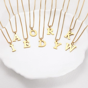 Detail of assorted gold initial necklaces on a white ceramic plate showing the box chain texture