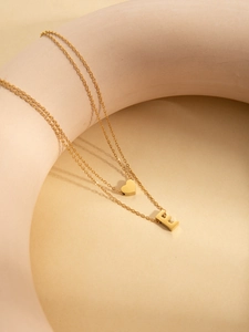 Detail of layered gold titanium necklace featuring a heart charm and a capital letter E