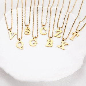 Detail of gold titanium steel initial necklaces with box chains on white wavy tray