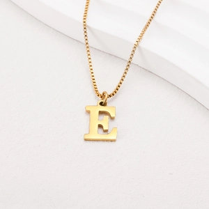 Detailed view of gold-plated letter E pendant with polished venetian chain on white steps