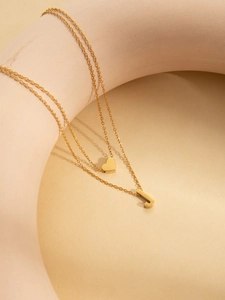 Detailed view of layered gold necklace with heart and letter J pendants on minimalist background
