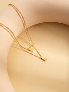 Detail of double-layer gold necklace with heart pendant and letter L on a ceramic stand